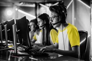 Mensen met koptelefoon op hun hoofd aan het werk achter hun computer. Ze dragen witte shirts met korte gele mouwen.