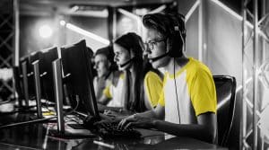 Mensen met koptelefoon op hun hoofd aan het werk achter hun computer. Ze dragen witte shirts met korte gele mouwen.